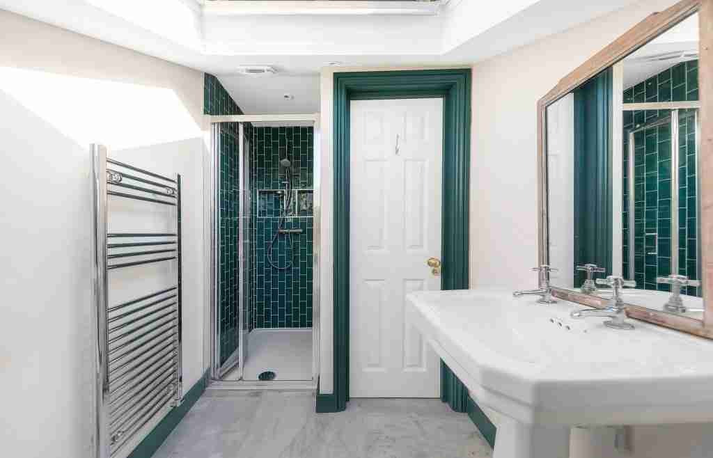 Bathroom with teal tiled shower, twin basins and heated towel rail after a home transformation