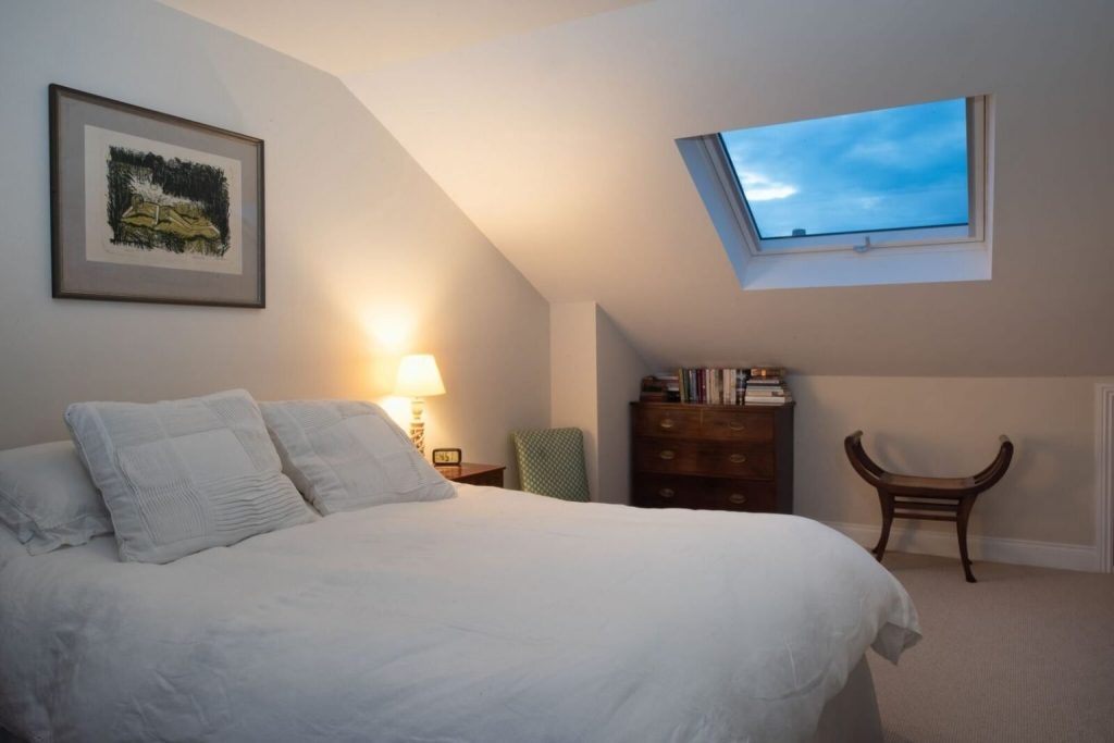 Loft conversion bedroom in London with sloped ceiling and warm bedside lighting