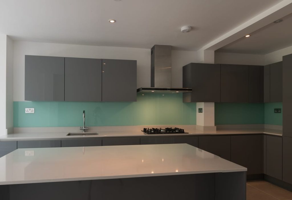 Ready to fit kitchen with grey island and green glass splashback in Fulham