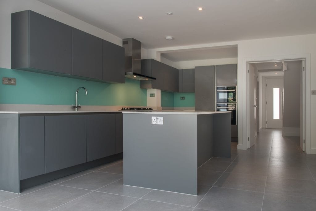 Grey kitchen island with dark green splashback fitted in a Fulham home